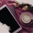 Auf einem Tuch liegen ein E-Reader, Blumen und steht eine Tasse mit Kaffee